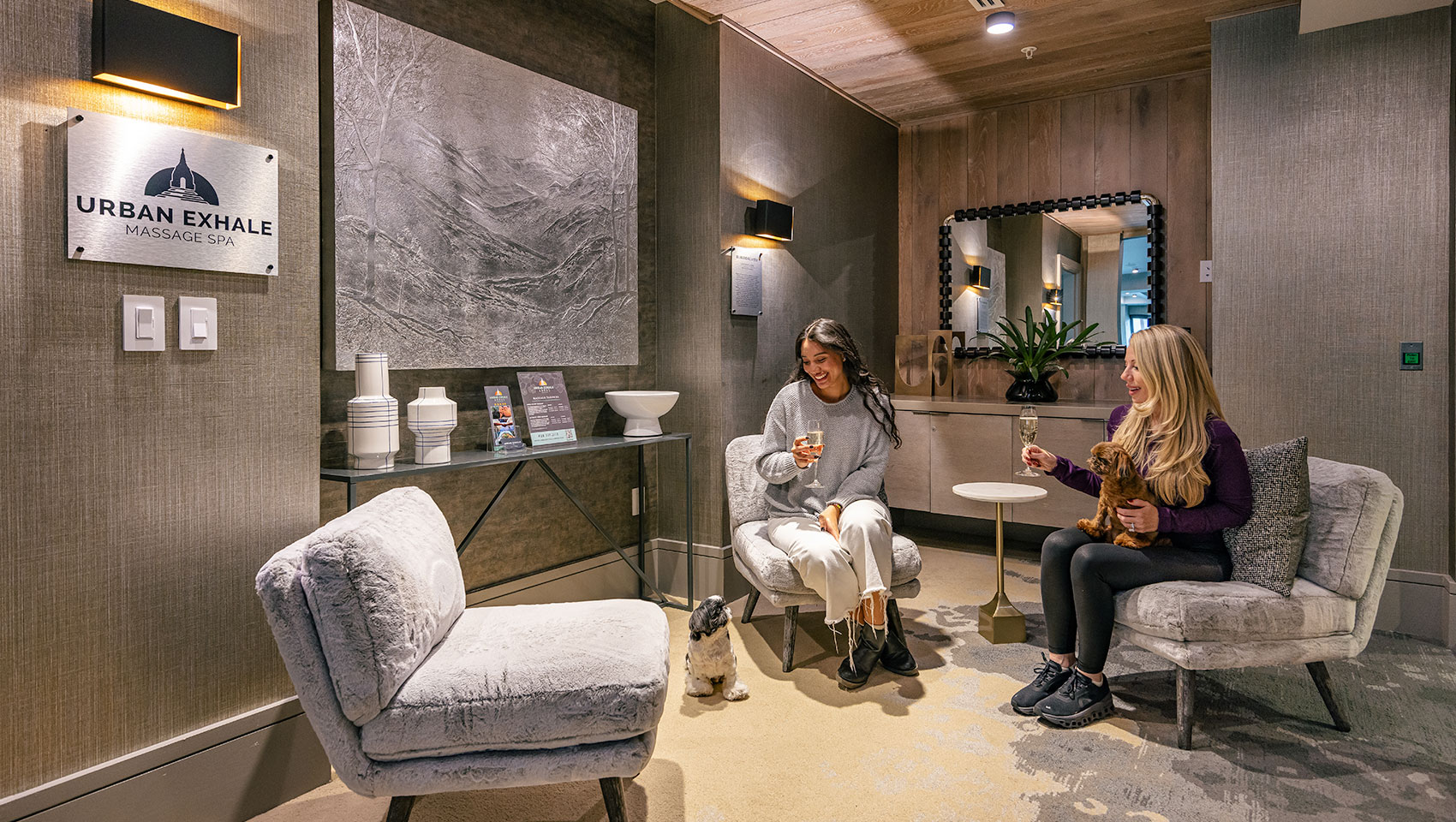 Two women holding dogs and a glass of champagne at Urban Exhale Massage